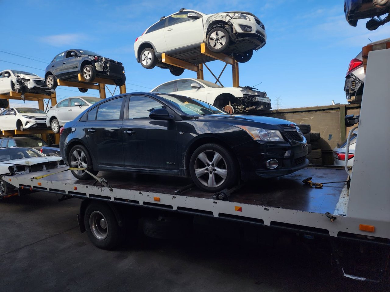 Dark sedan loaded on a flatbed truck in a vehicle yard