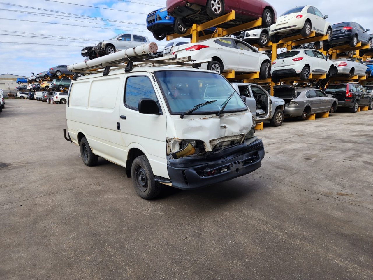 White van parked beside dismantling-yard vehicles